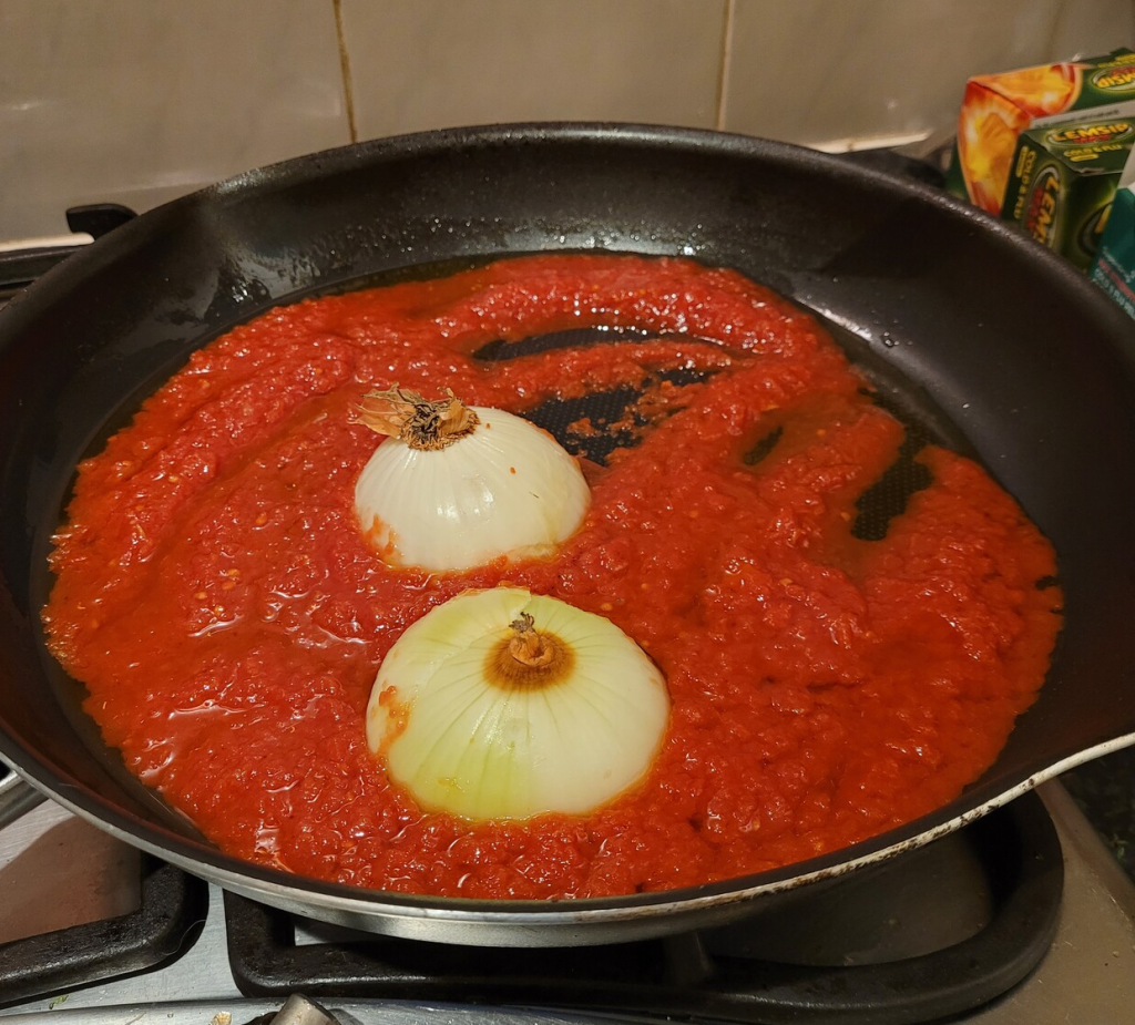 Two halved onions in a pan of chopped tomatoes